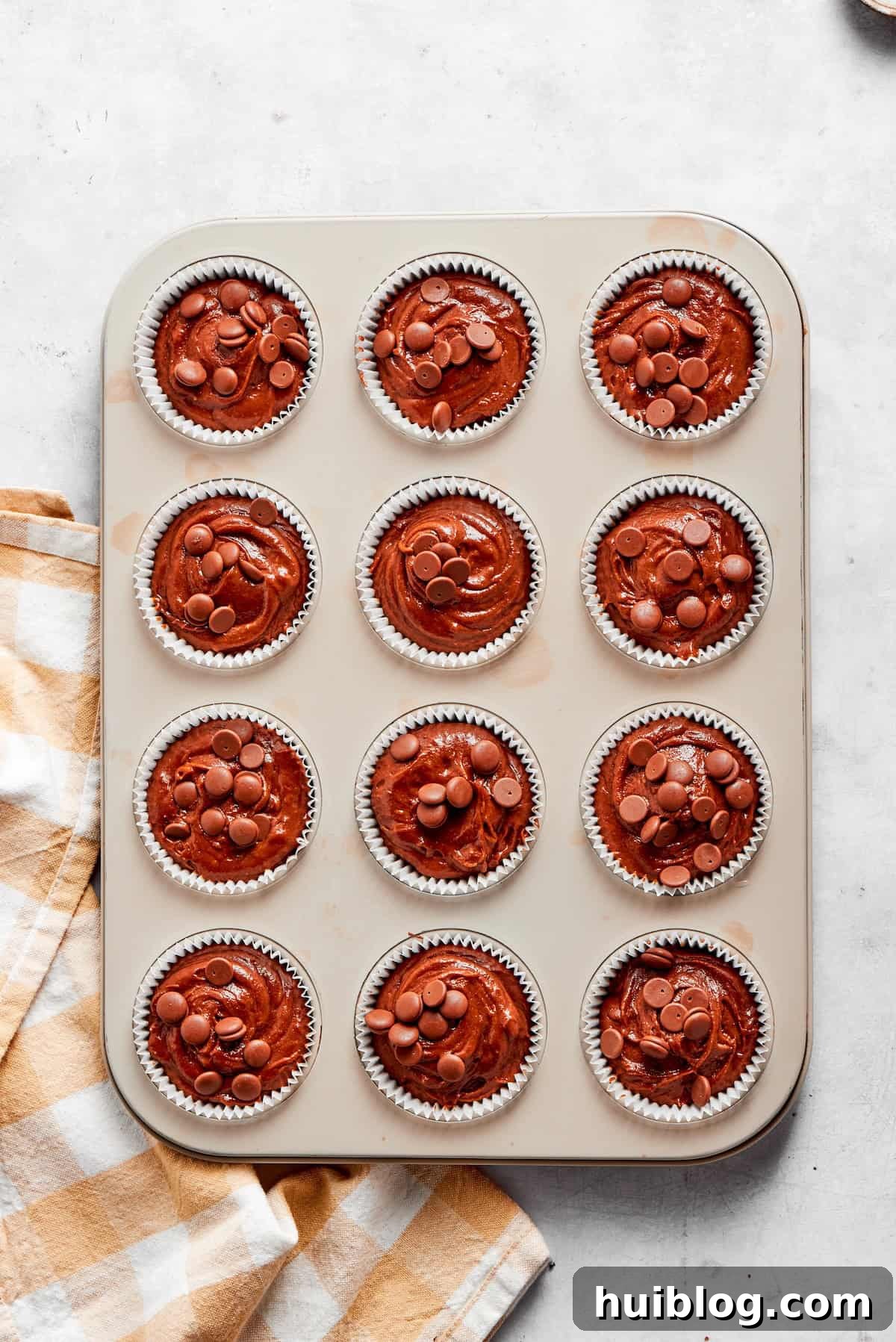 Chocolate muffin batter being divided evenly into a muffin tin lined with paper cups.