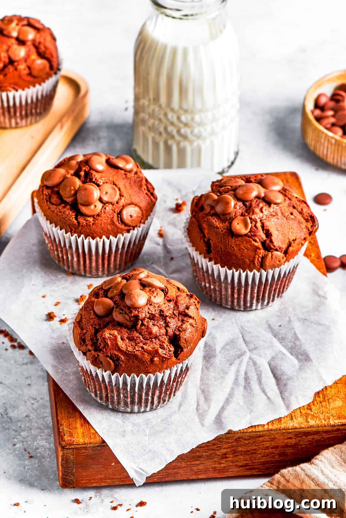 Finished double chocolate muffins beautifully arranged on a wooden board, with a blurred glass of milk in the background.