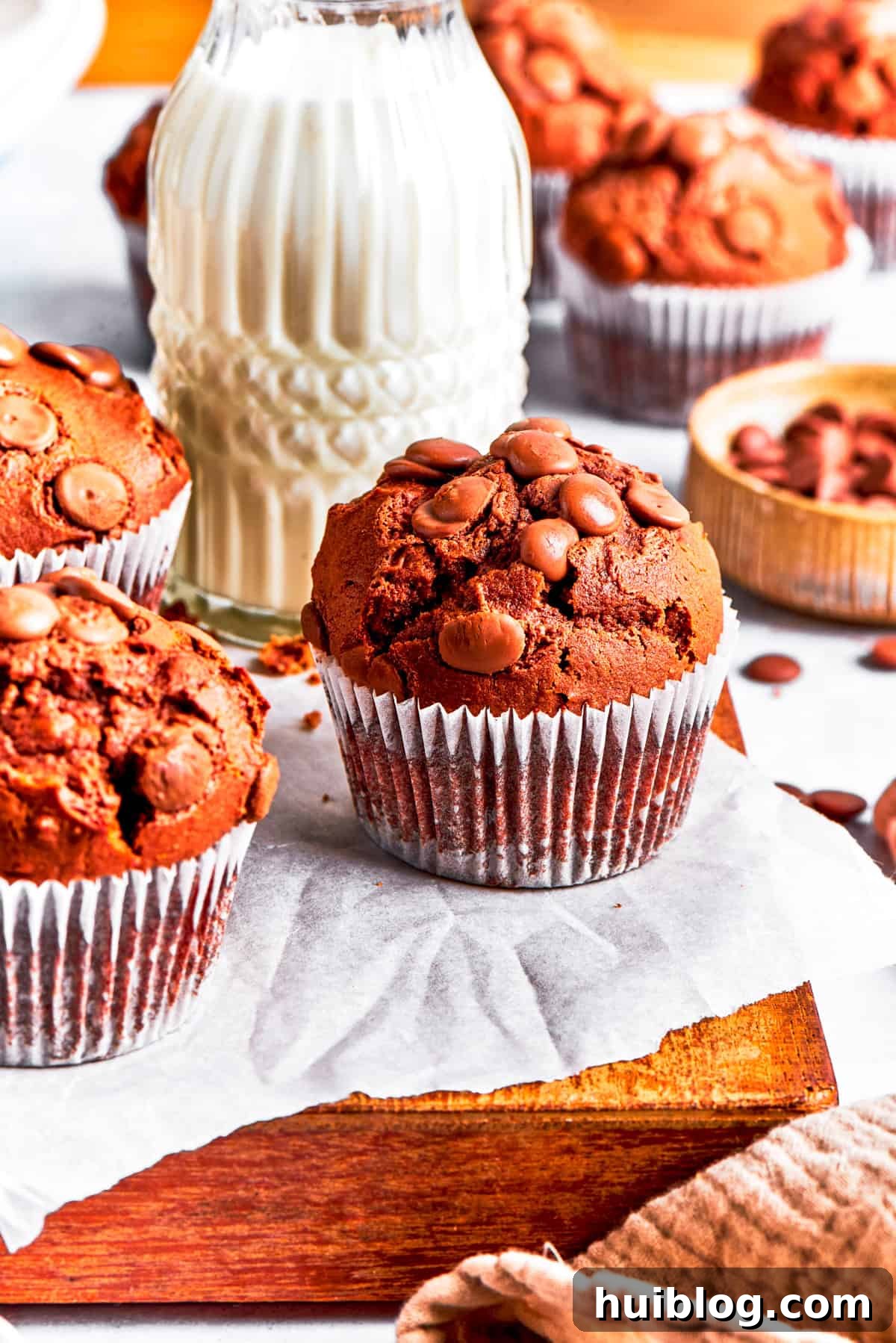 Freshly baked double chocolate muffins served on a rustic wooden board with a glass of milk in the background.