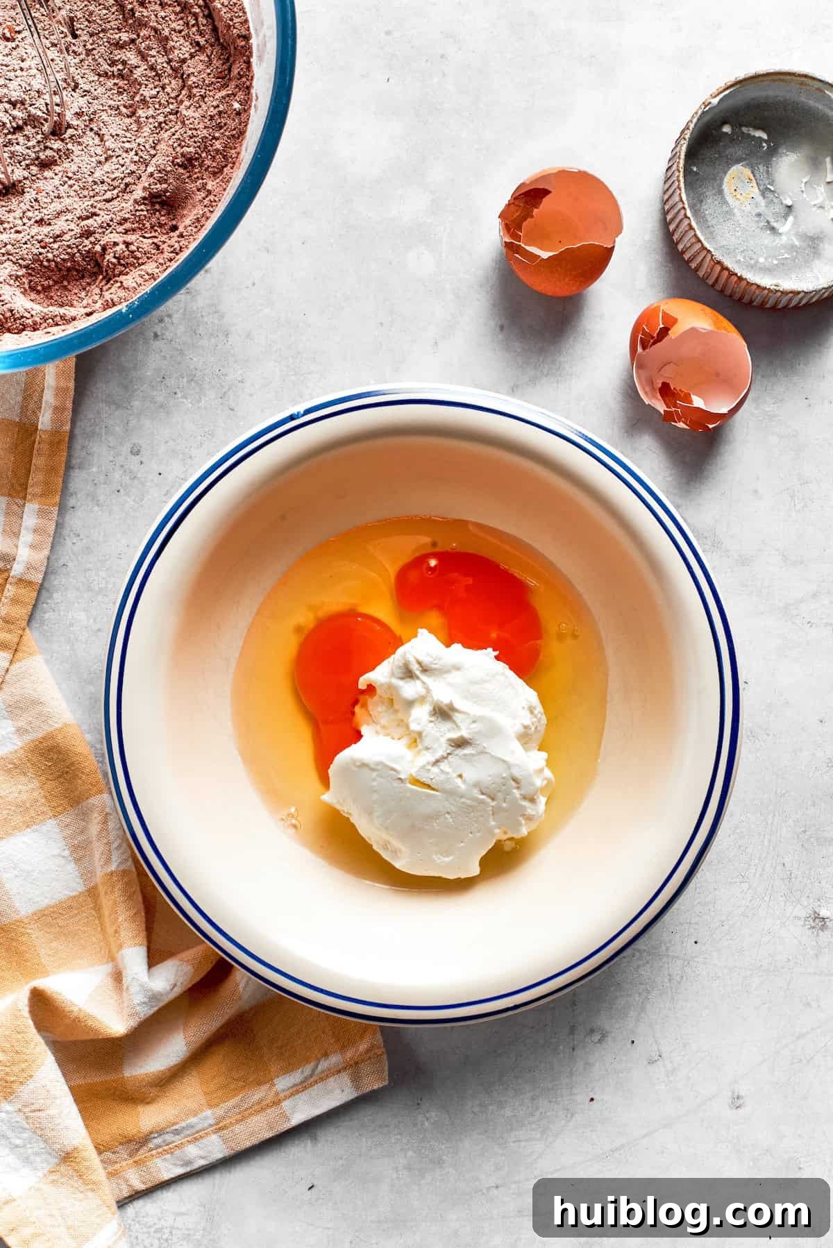 Eggs are expertly whisked with sour cream in a mixing bowl for chocolate muffins.