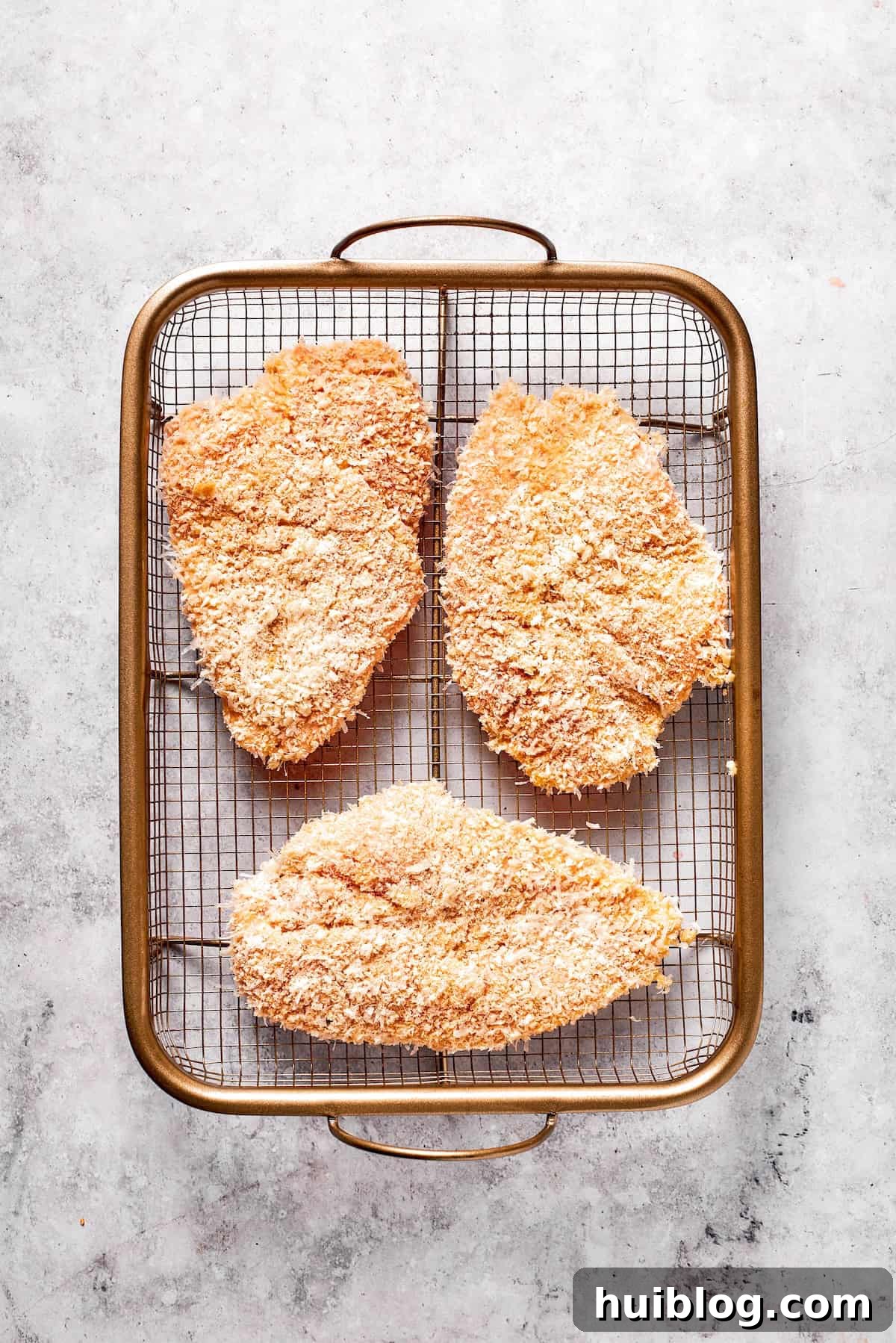 Three fully breaded chicken cutlets arranged on a clean plate, ready for frying, showcasing their uniform coating.