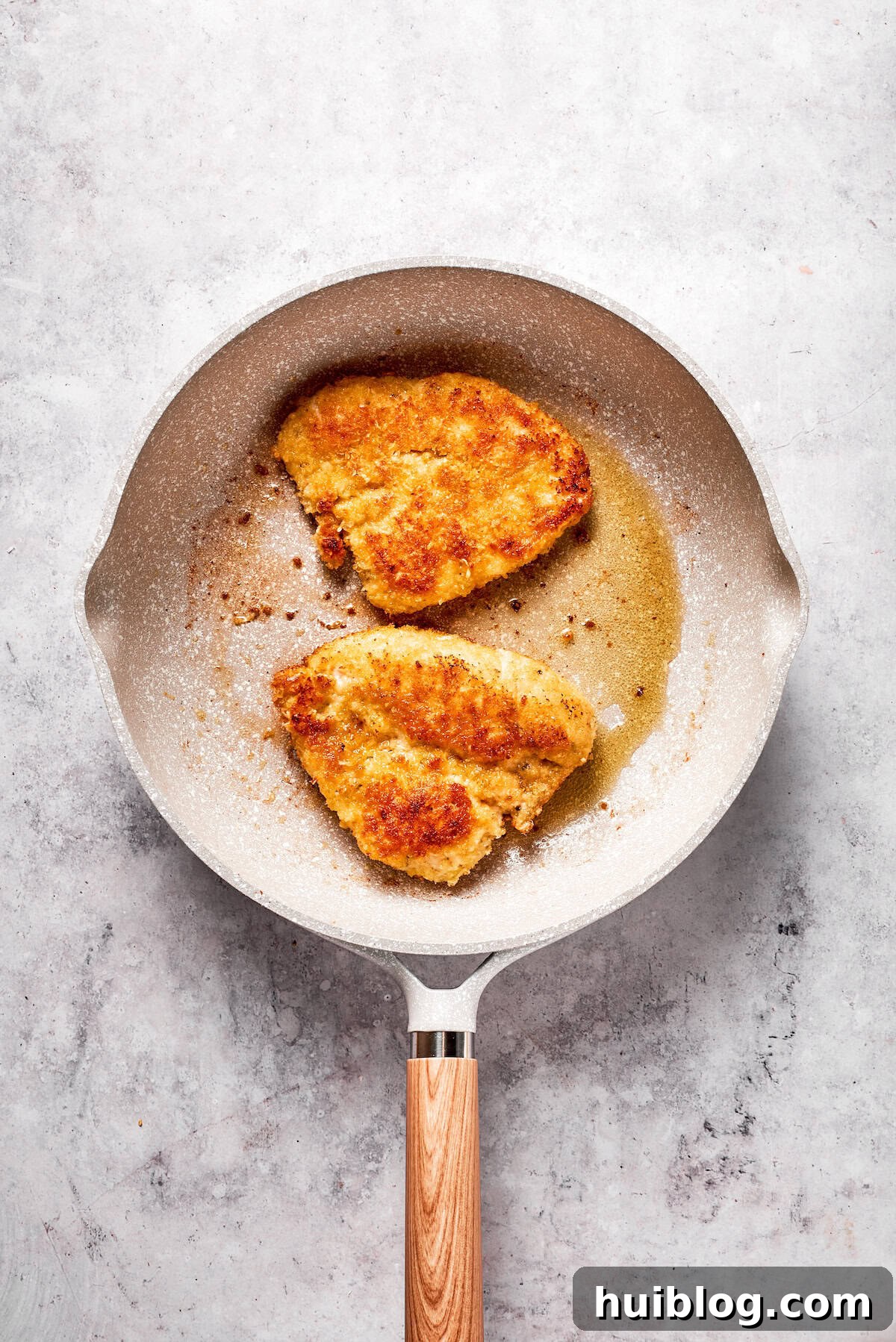 Two breaded chicken cutlets sizzling and turning golden brown in a hot skillet with oil.