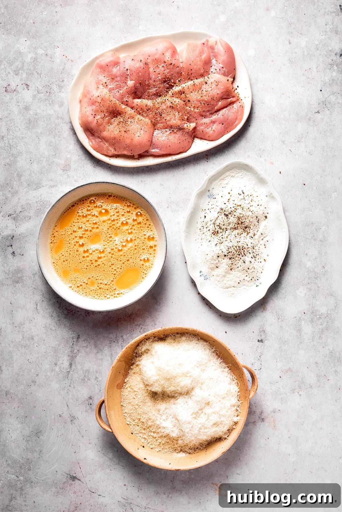 Three shallow bowls arranged for dredging: one with flour mixture, one with whisked eggs, and one with breadcrumbs and cheese.