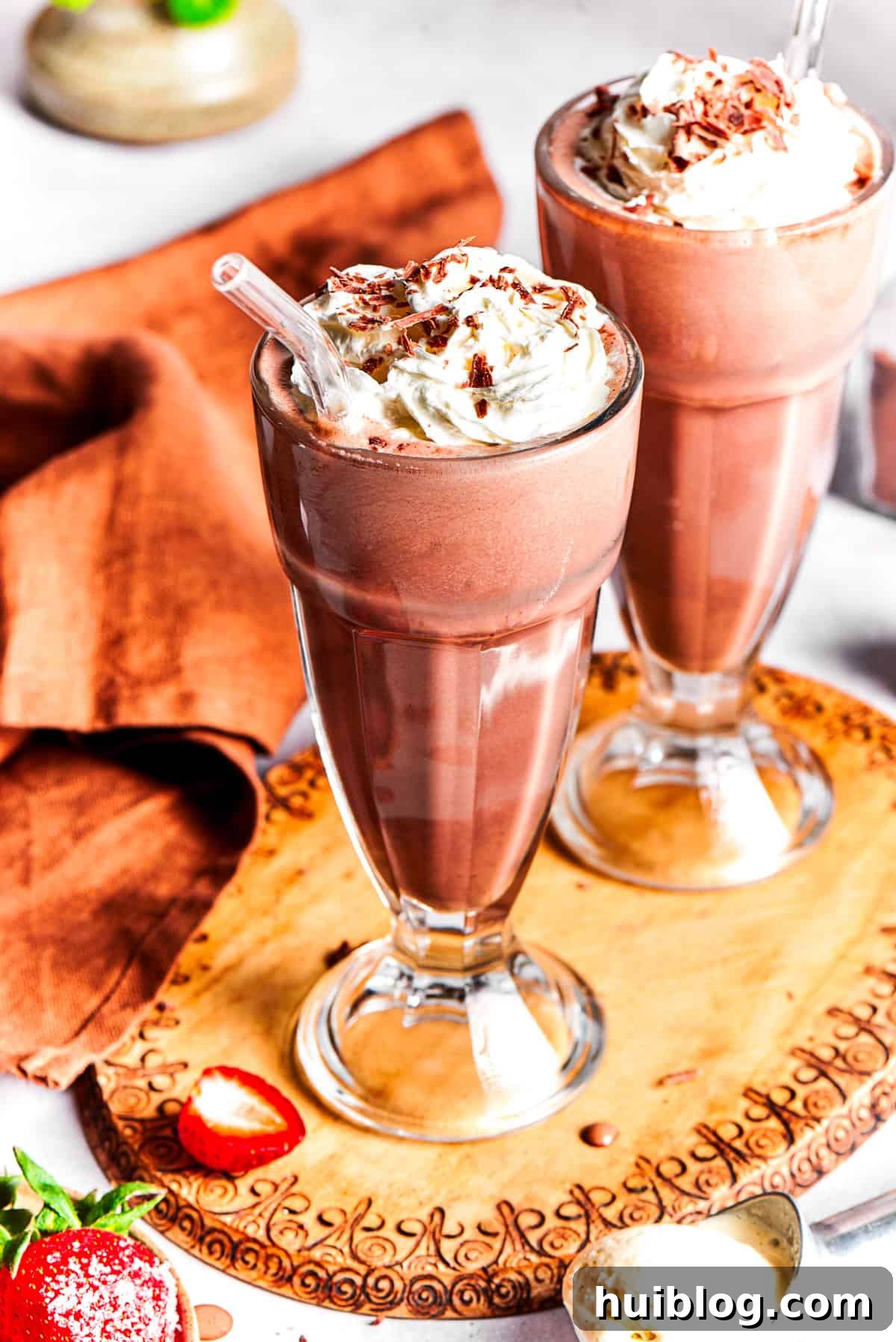 Two inviting glasses of chocolate milkshake, beautifully garnished with whipped cream, fresh strawberries, and chocolate drizzle, resting on a rustic wooden tray, ready for immediate enjoyment.
