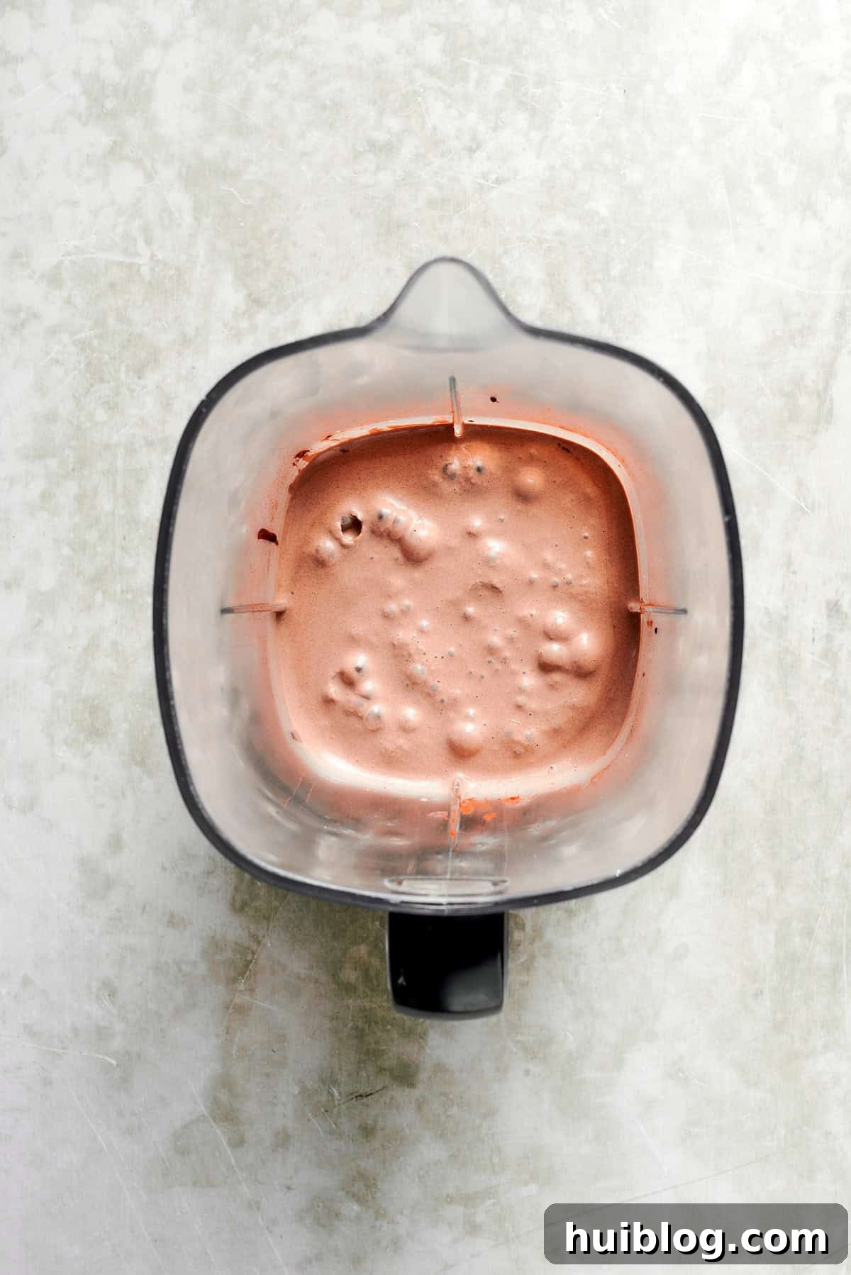 A blender actively mixes the ingredients for a chocolate milkshake, creating a smooth, swirling brown vortex, indicating a perfectly creamy consistency.
