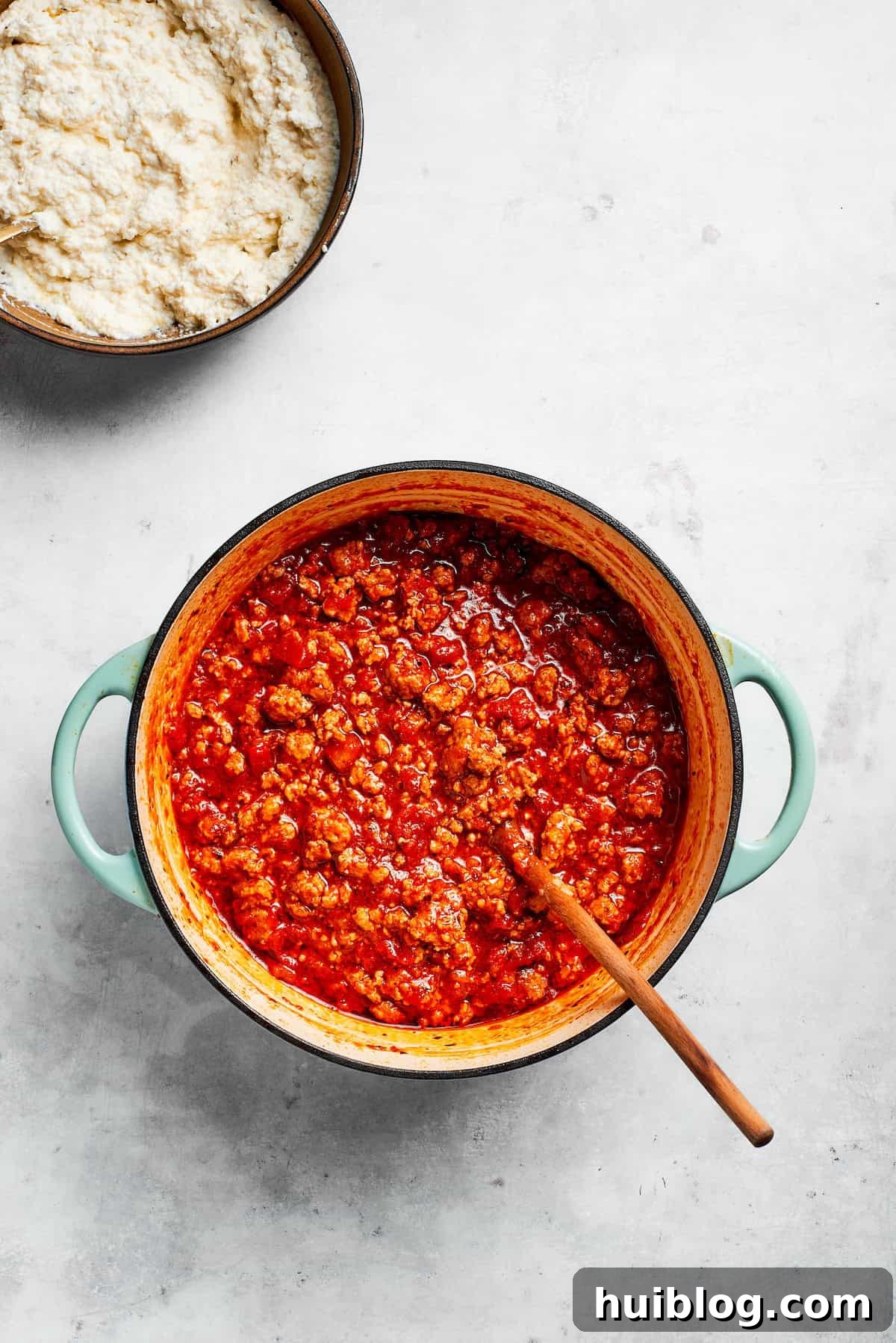 A rich, deep red beef and tomato sauce gently simmering in a large pot, covered, to develop its complex flavors.