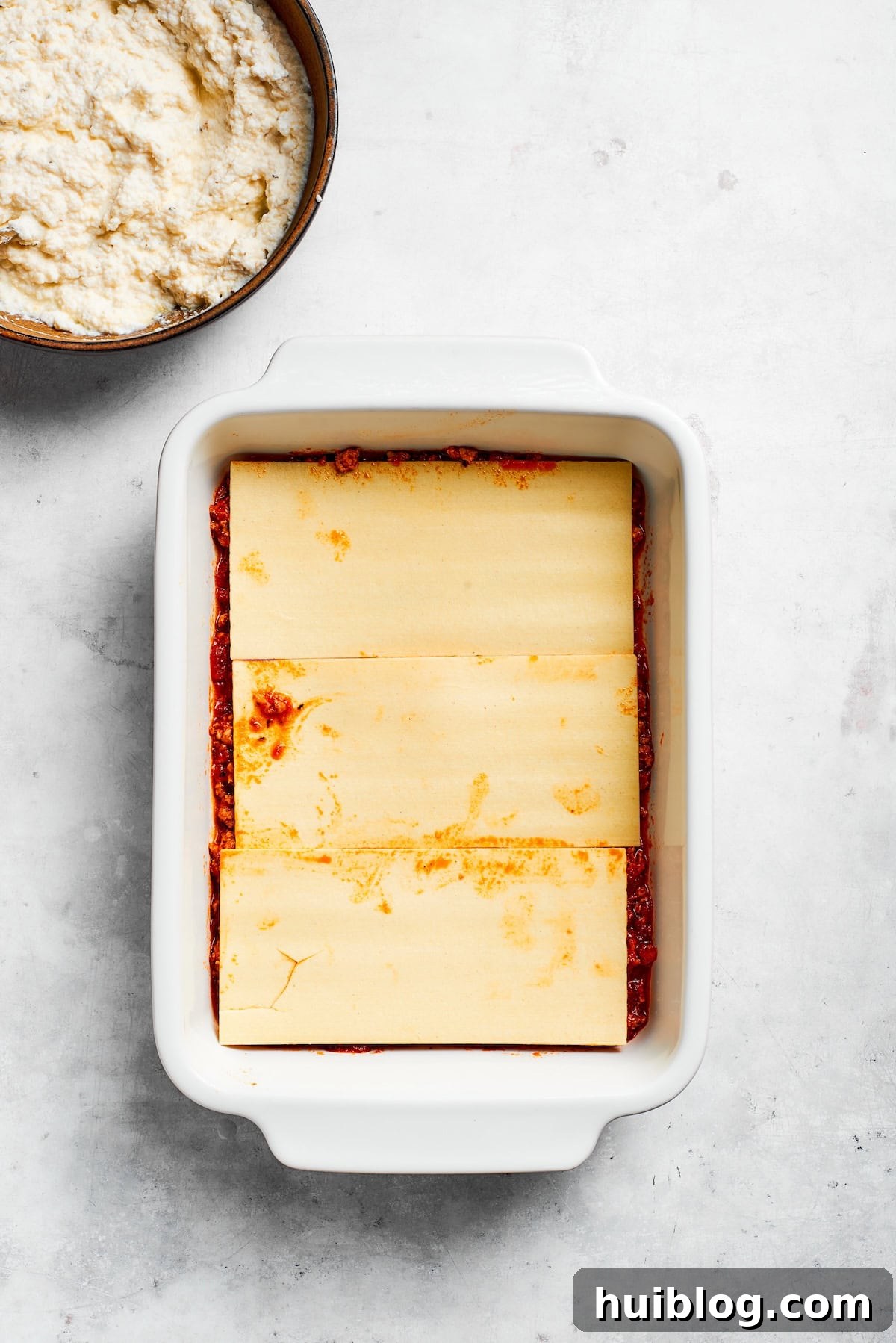 Cooked lasagna noodles neatly layered over a bed of meat sauce in a baking pan, forming the first pasta layer.