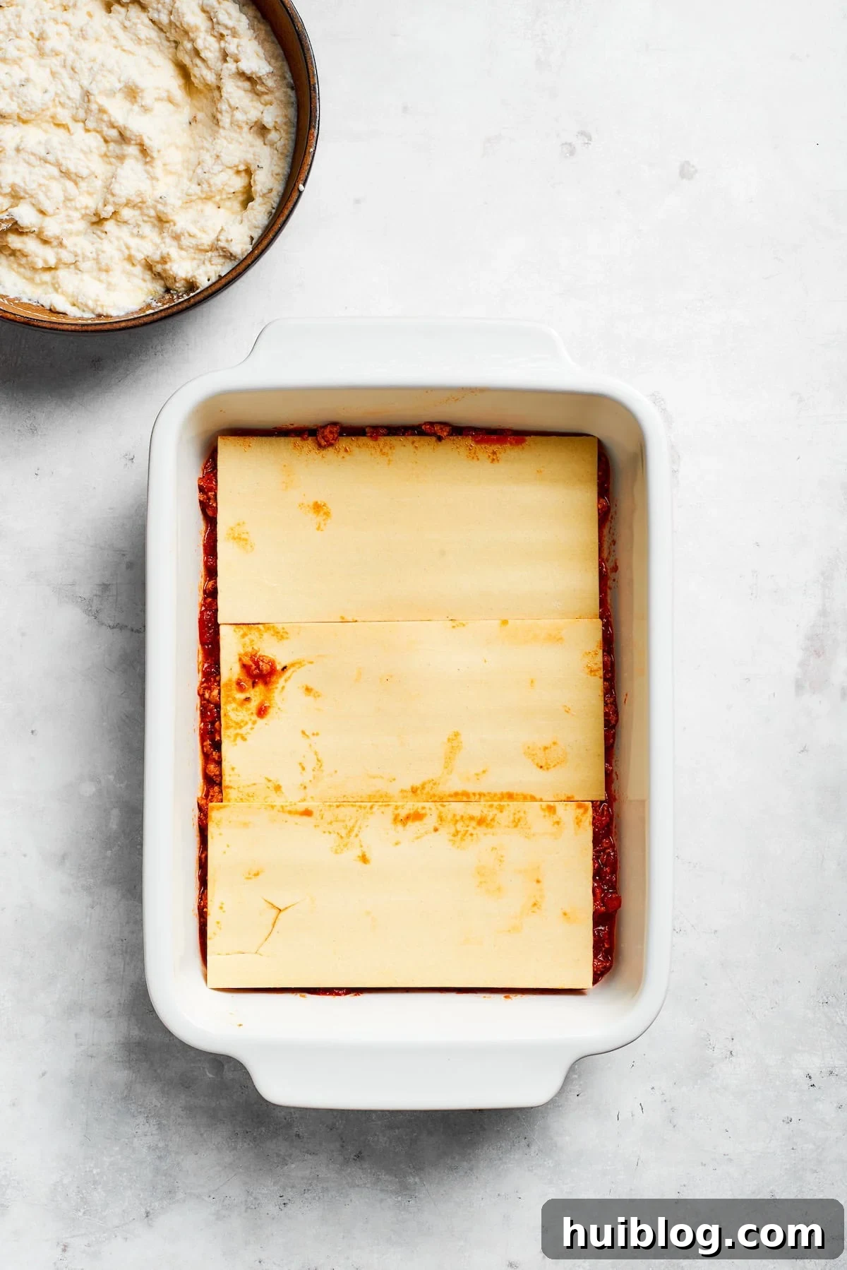 The first layer of cooked lasagna noodles arranged over a base of meat sauce in a baking dish.