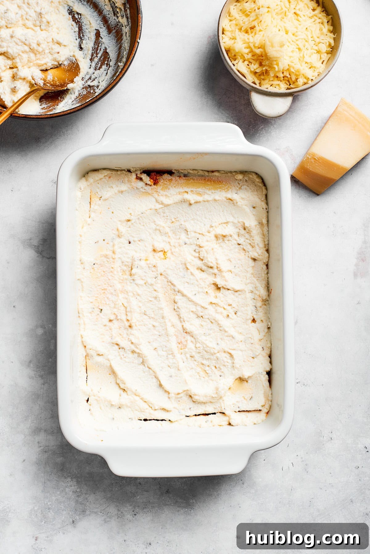 Creamy ricotta cheese mixture spread evenly over a layer of lasagna noodles in a baking dish.