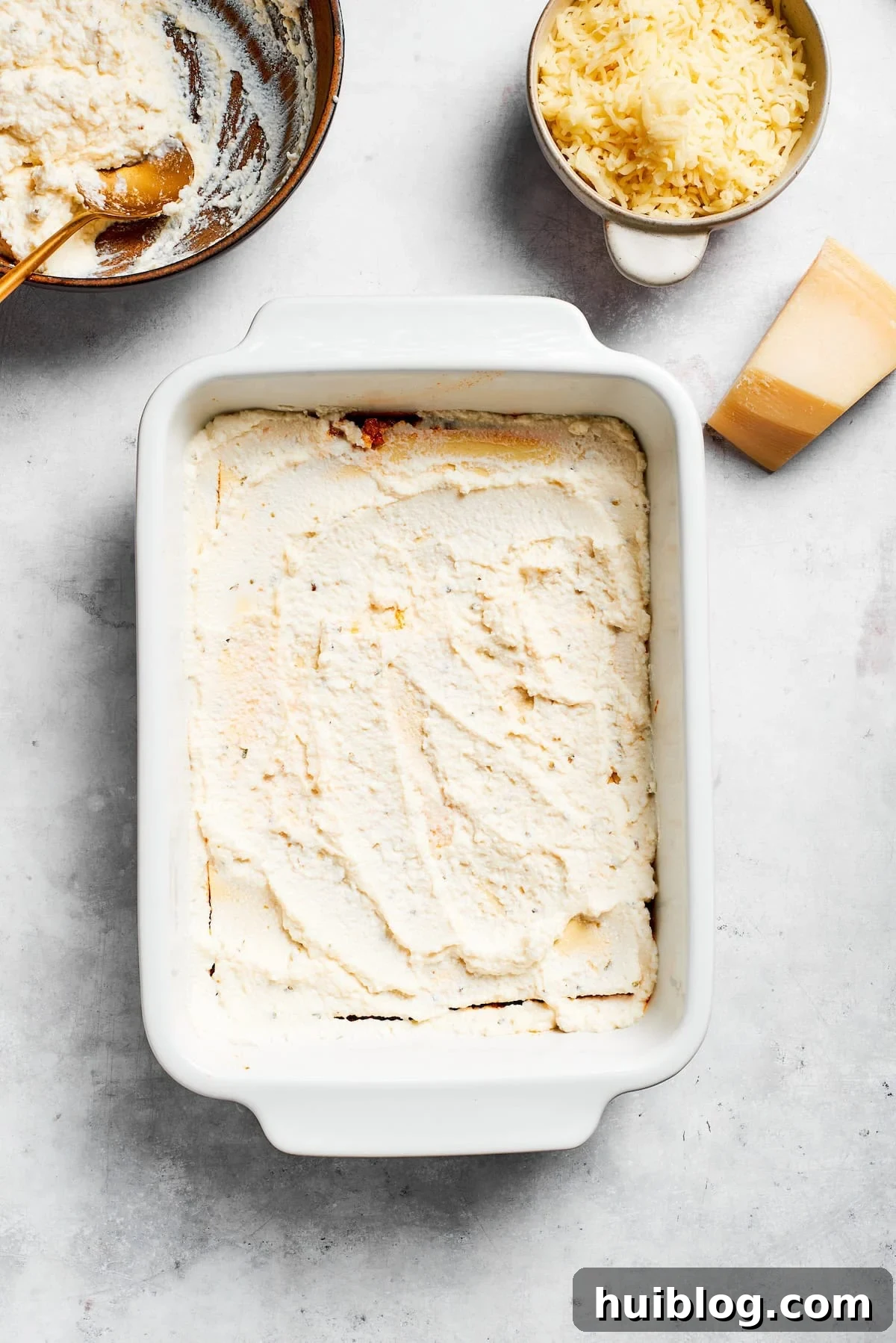 A layer of creamy ricotta cheese mixture spread evenly over lasagna noodles in a baking dish.