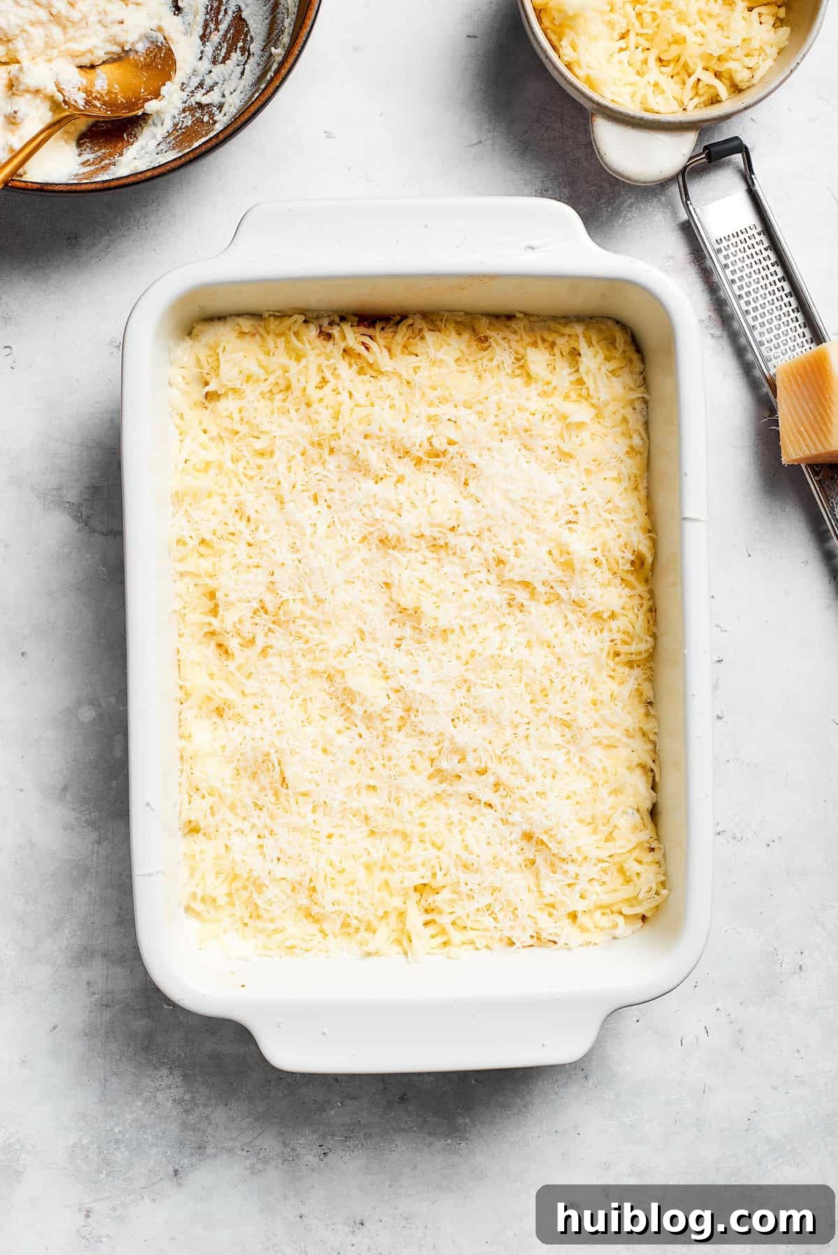 Shredded mozzarella and Parmesan cheese generously sprinkled over the ricotta layer in a lasagna pan.