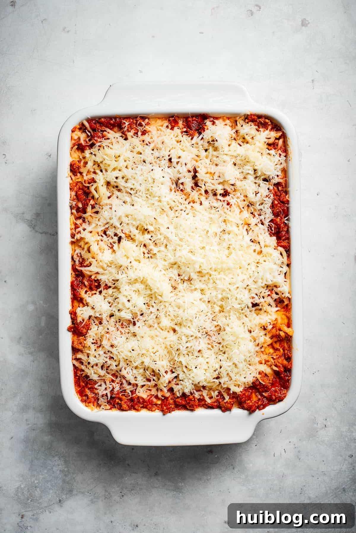 A full pan of beef lasagna, topped with a generous layer of shredded cheese, ready for baking.