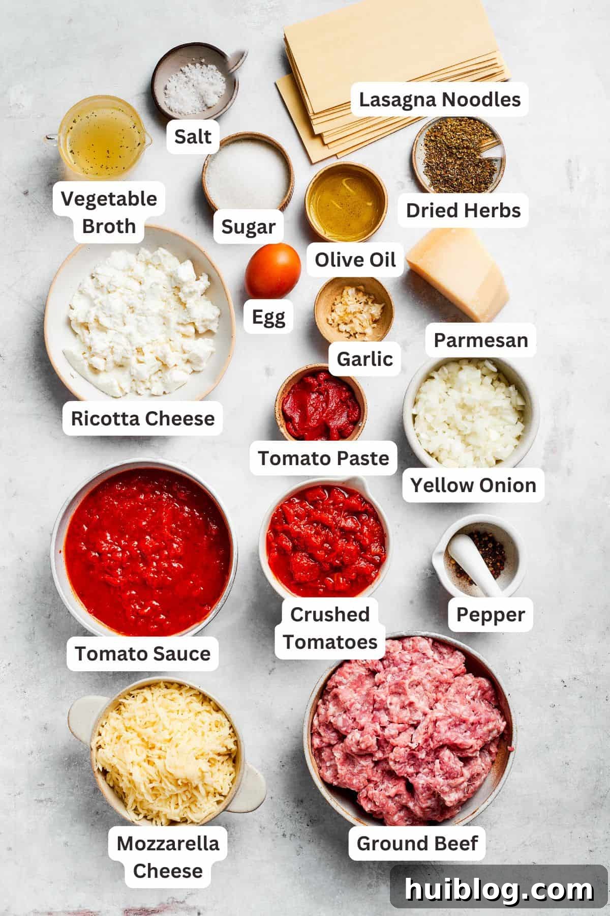 Various fresh ingredients for beef lasagna laid out on a wooden board, including ground beef, tomatoes, cheese, onions, and herbs.