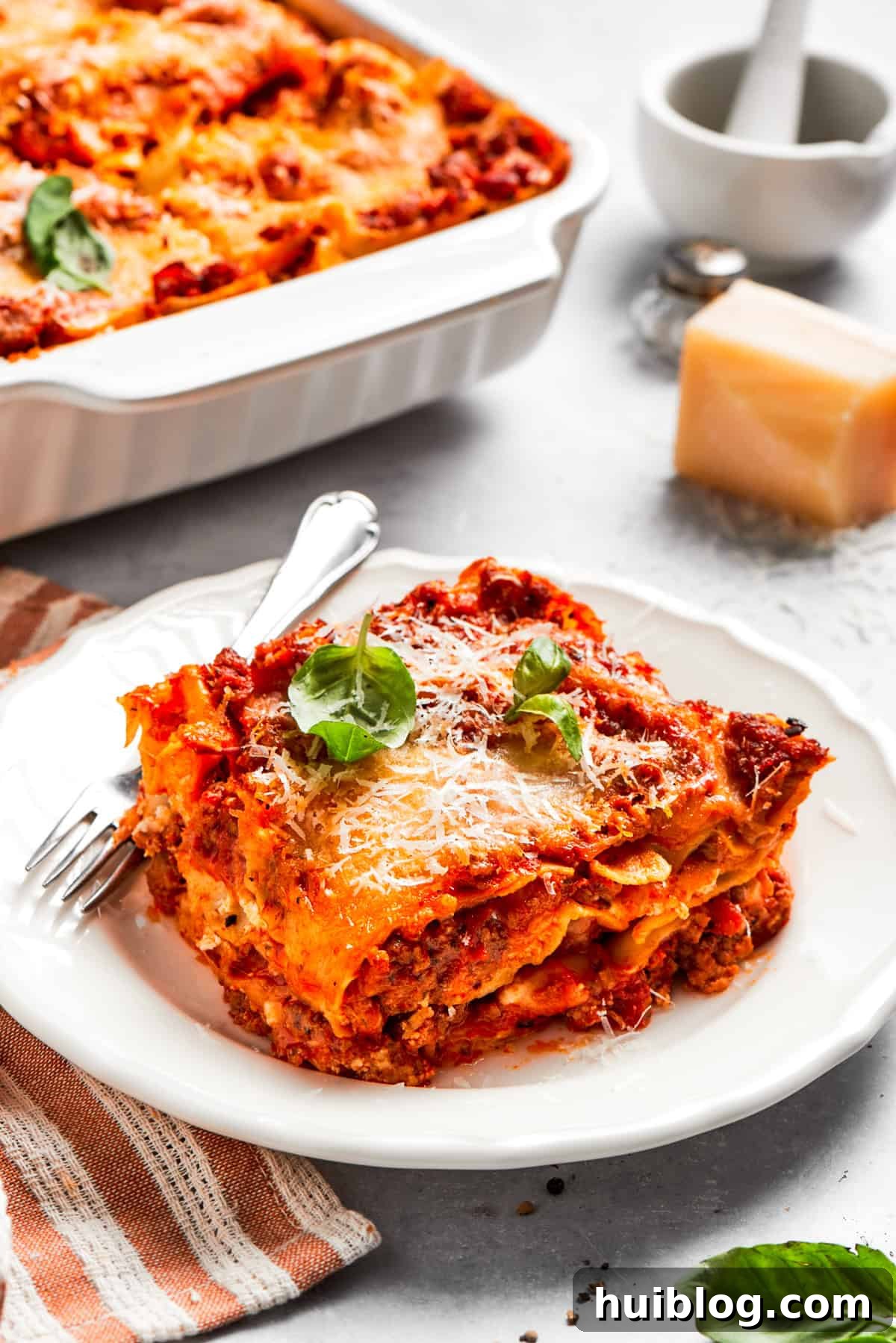 A generous serving of homemade beef lasagna, perfectly cut and presented on a dinner plate with a fork, ready to be enjoyed.
