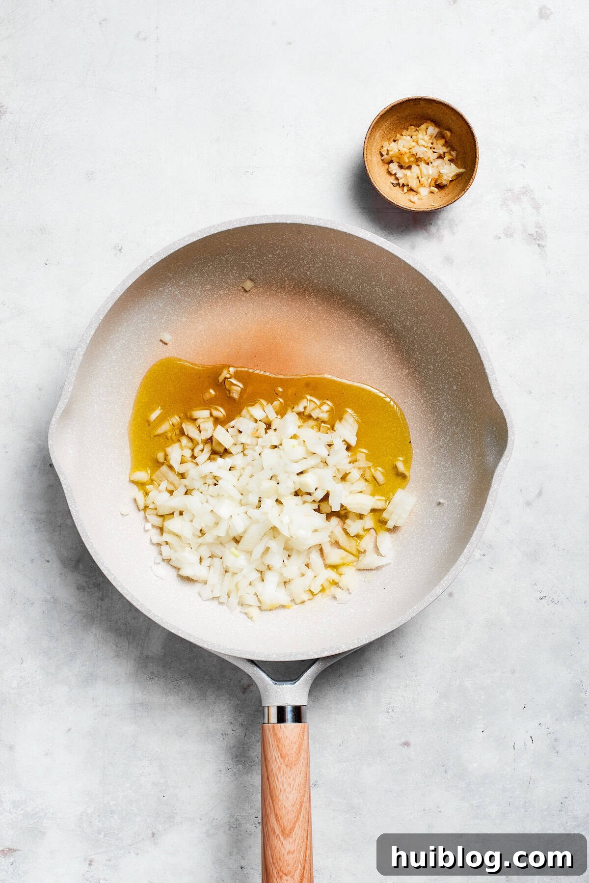 Diced yellow onions and minced garlic gently sautéing in shimmering olive oil in a skillet, creating an aromatic base.