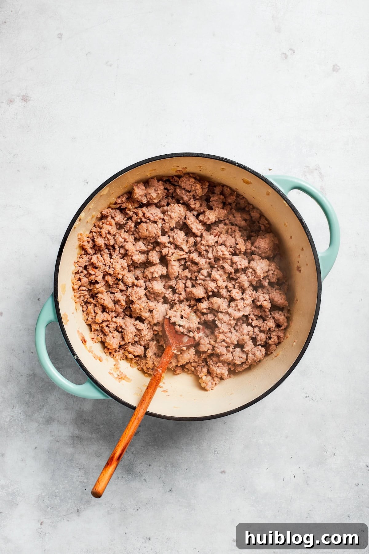 Ground beef browning in a skillet, stirred with a spoon to break it apart and ensure even cooking.