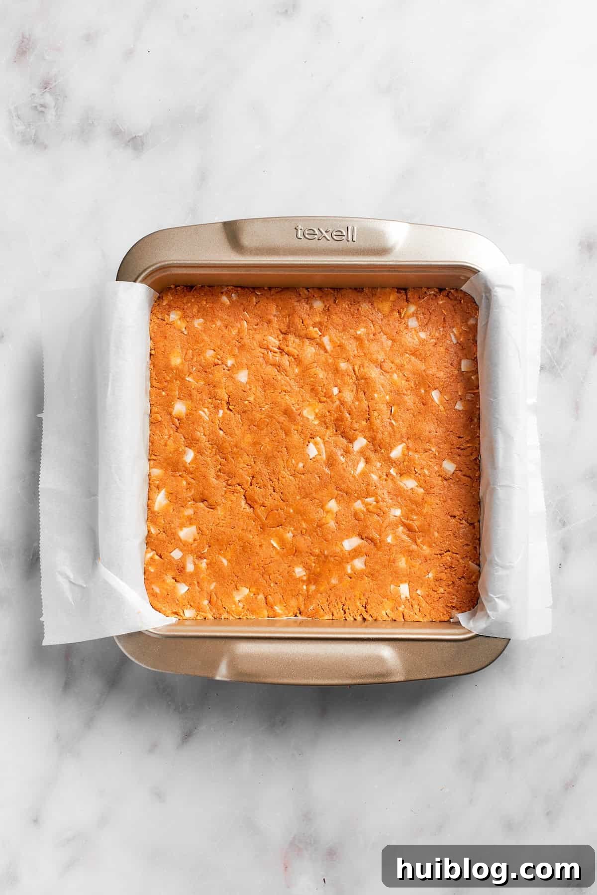 The graham cracker crust mixture firmly pressed into a lined square baking pan, ready for chilling.