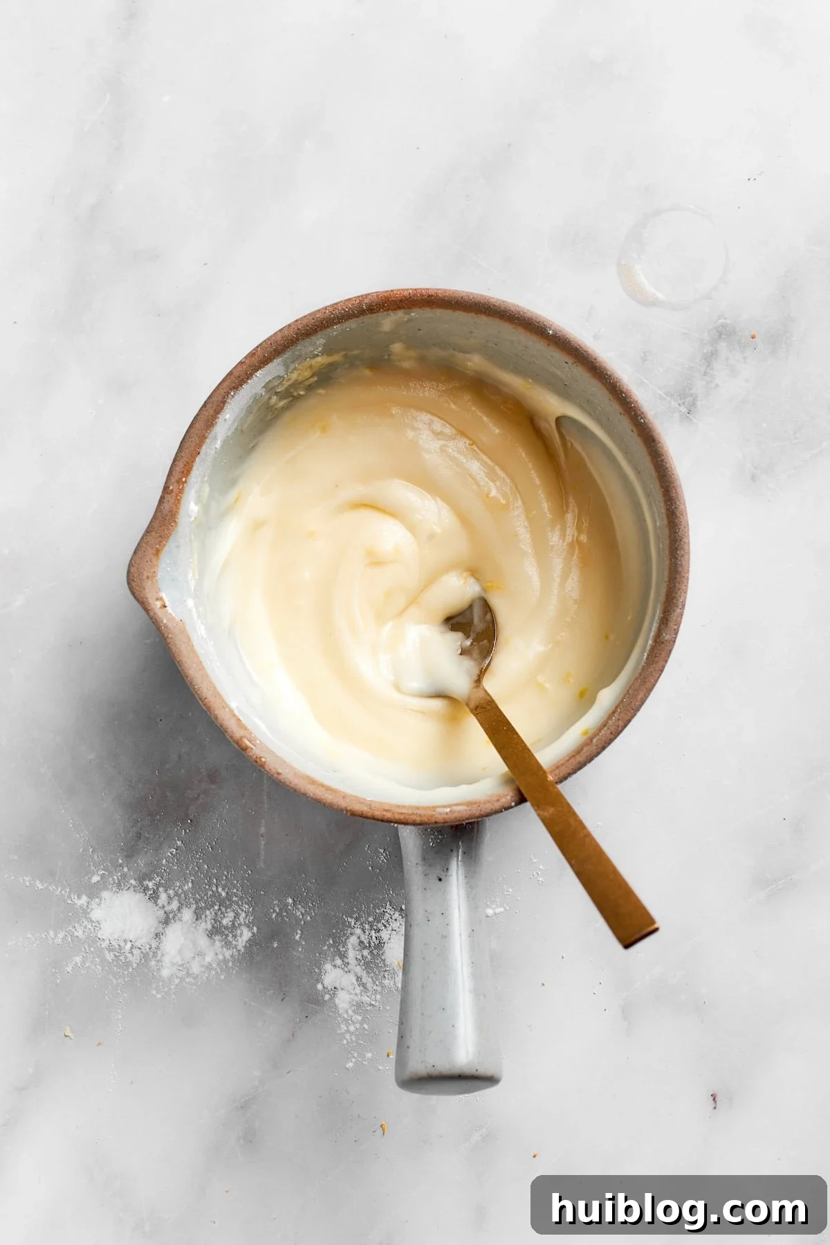 A spoon stirring the lemon frosting in a bowl, showing its thick, spreadable consistency.