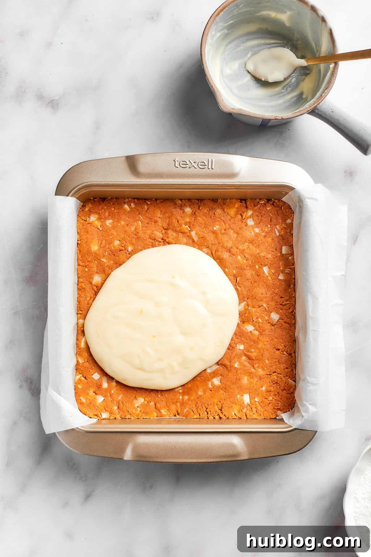 The vibrant lemon frosting being spread evenly over the chilled graham cracker crust in a baking pan.