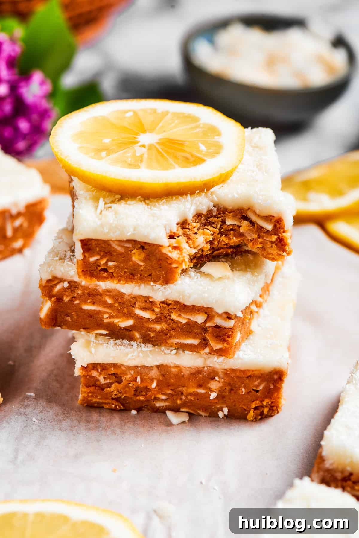 Three perfectly cut lemon slice squares, stacked neatly, with one having a bite taken out of it, showing the layers.