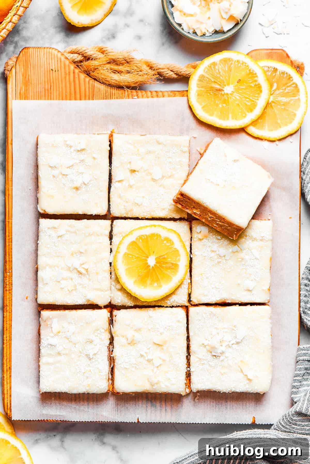 Rows of perfectly cut lemon slice squares topped with a smooth, glossy frosting and a sprinkle of coconut.
