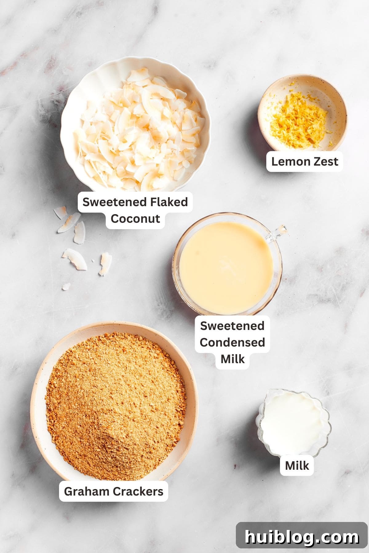 An array of fresh ingredients for lemon slice, including lemons, graham crackers, coconut, and condensed milk.