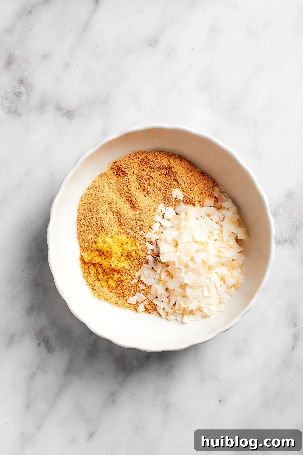 Sweetened coconut flakes being added to a bowl of finely crushed graham crackers.