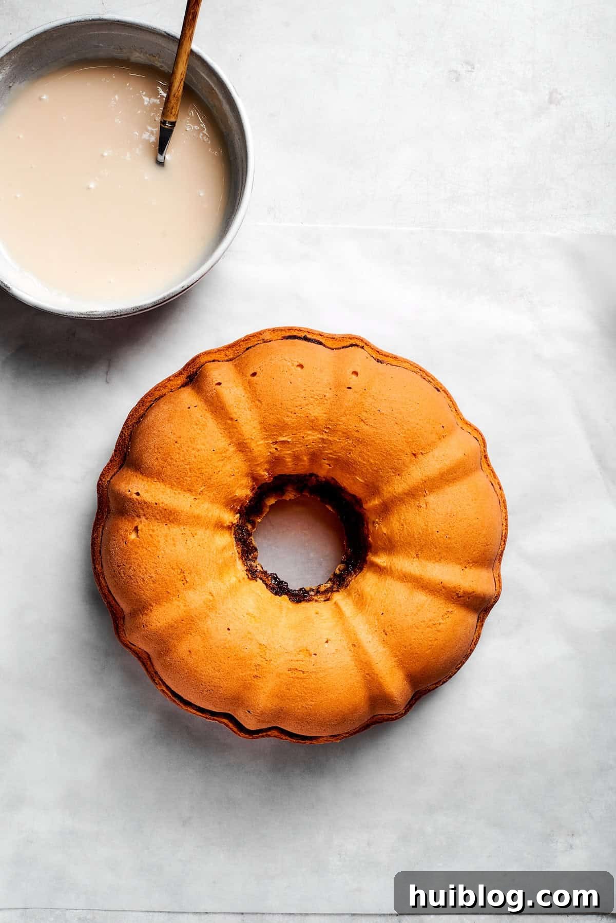 A bowl of icing next to a cooled cake.