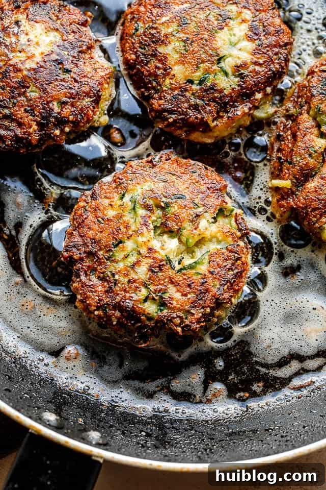 Golden Zucchini Fritters 4 Golden-brown zucchini fritters frying in a black skillet, sizzling in hot oil.