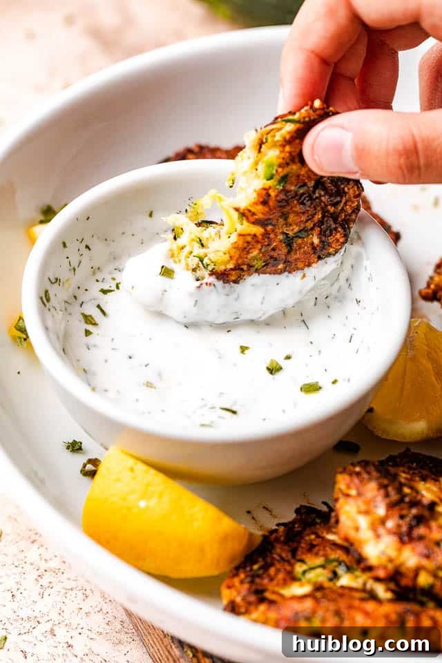 Golden Zucchini Fritters 6 A crispy zucchini cake being dipped into a creamy, herb-flecked yogurt or sour cream dip.