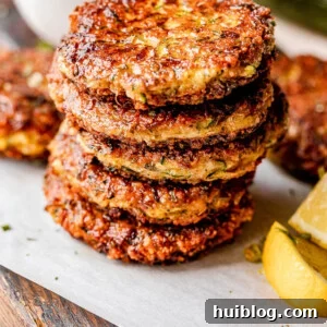 Stacked crispy zucchini fritters with fresh lemon wedges and a creamy sour cream dip in the background.