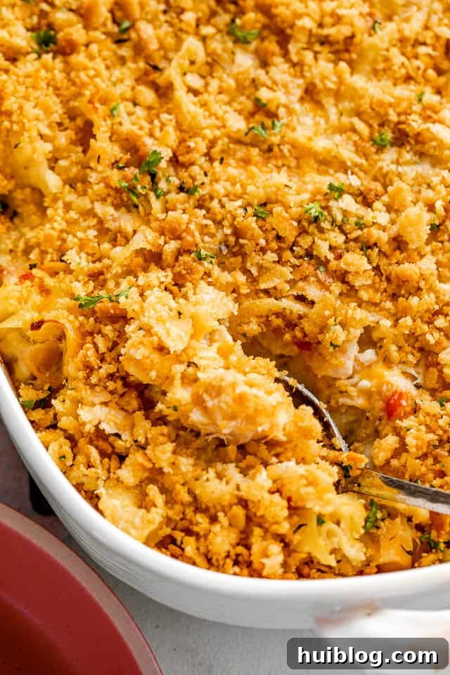This Tuna Noodle Casserole is a creamy, cheesy, and comforting dish made from scratch, perfect for an easy and satisfying weeknight dinner. silver spoon cutting into a tuna noodle casserole topped with ritz crackers
