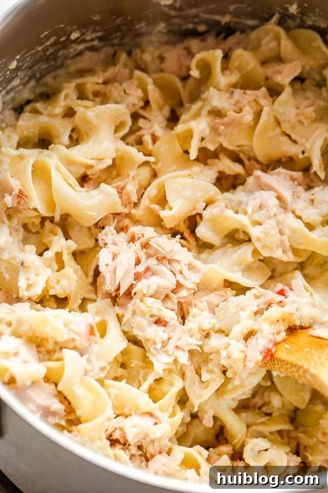 This Tuna Noodle Casserole is a creamy, cheesy, and comforting dish made from scratch, perfect for an easy and satisfying weeknight dinner. a pot filled with cooked egg noodles mixed with canned tuna