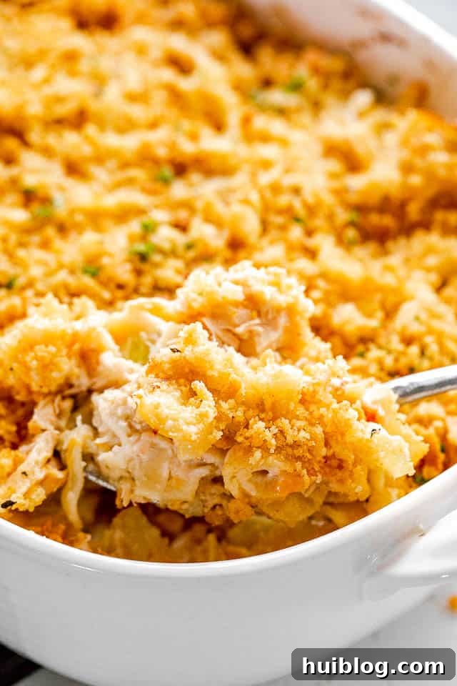 This Tuna Noodle Casserole is a creamy, cheesy, and comforting dish made from scratch, perfect for an easy and satisfying weeknight dinner. scooping out tuna noodle casserole from baking dish