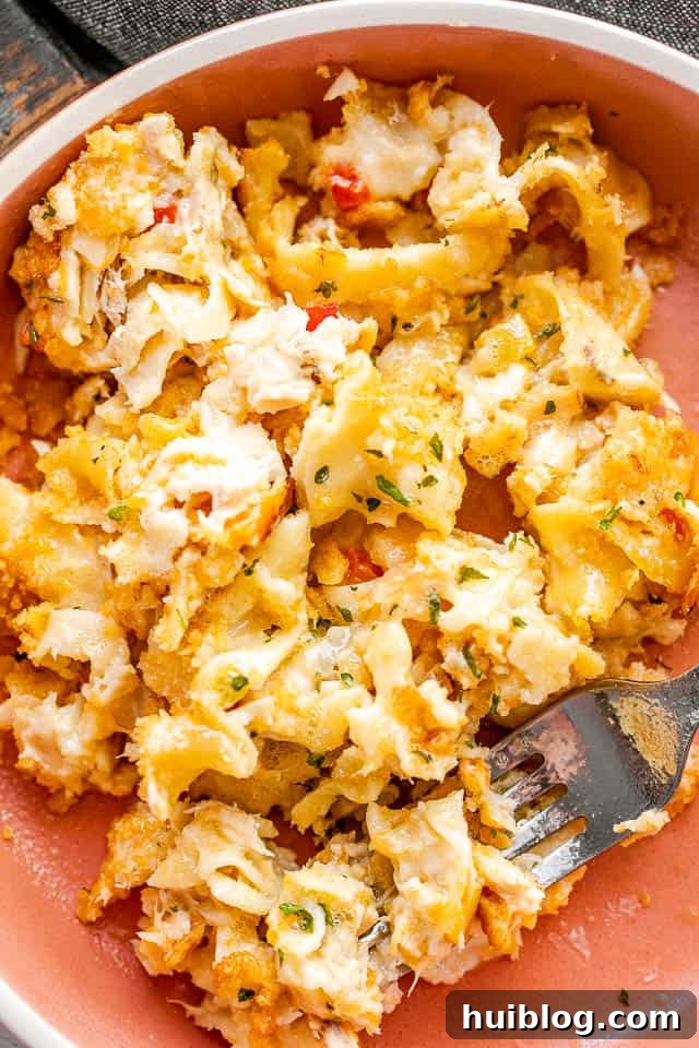 This Tuna Noodle Casserole is a creamy, cheesy, and comforting dish made from scratch, perfect for an easy and satisfying weeknight dinner. serving tuna noodle casserole in an orange bowl with a silver fork