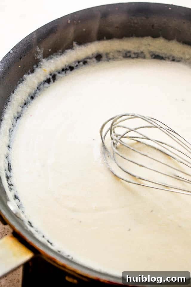 whisking cream cheese sauce in a black skillet, showing smooth texture