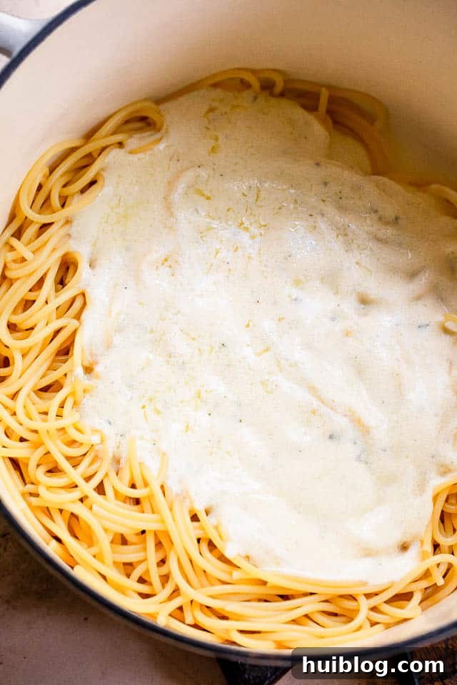 white dutch oven with spaghetti and white cream sauce on top, ready to mix