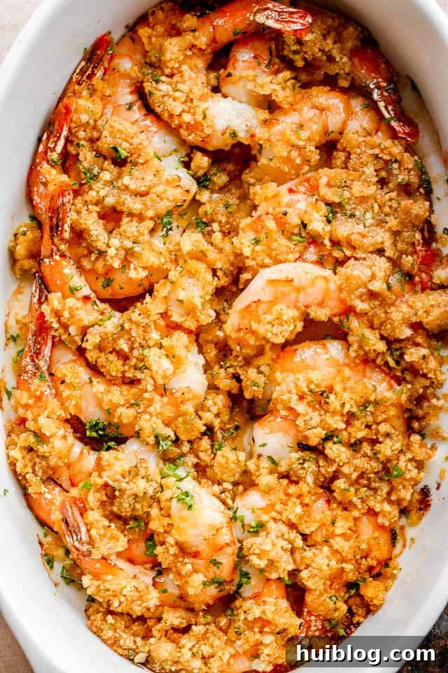 Shrimp Delectables: Garlic Butter Baked and De Jonghe 2 overhead shot of arranged shrimp in a white oval dish and topped with garlic butter and breadcrumbs mixture.