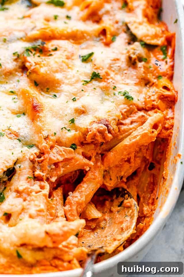 Velvety Zucchini Mushroom Pasta Bake 5 A side view of the cheesy baked pasta in a white baking dish, with a serving spoon scooping out a generous portion, showcasing the creamy texture and melted cheese.
