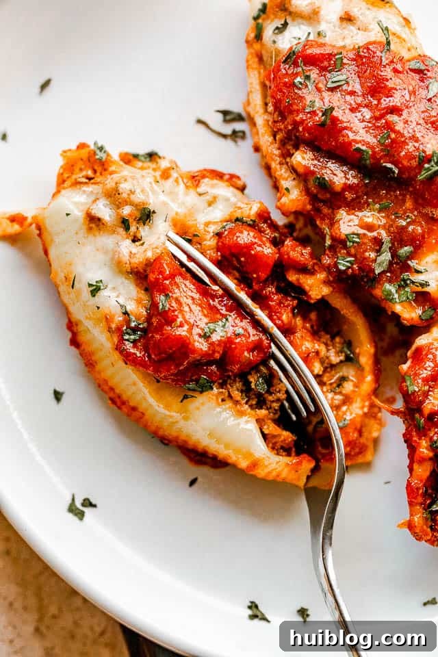Stuffed pasta shells with a savory beef and ricotta filling, baked in marinara and topped with melted cheese. It’s like lasagna in shells! cutting into stuffed pasta shells with a fork