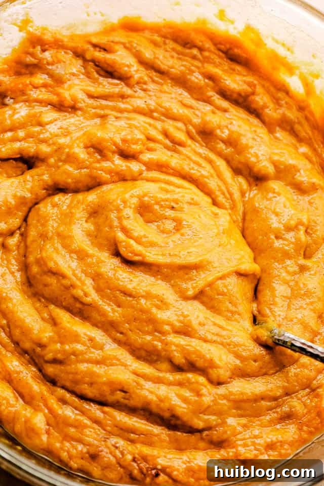 A mixing bowl filled with smooth, vibrant orange pumpkin puree, ready to be incorporated into the cake batter.