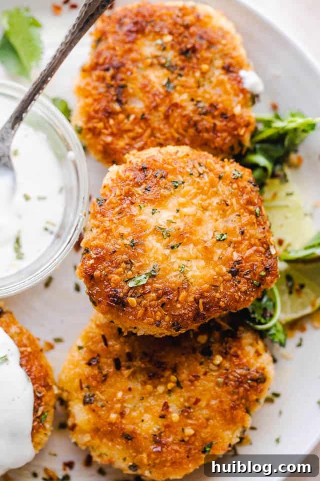 Golden Coconut Shrimp Patties 6 Close-up overhead shot of beautifully plated coconut shrimp cakes on a white serving plate, with a small bowl of sauce ready for dipping.