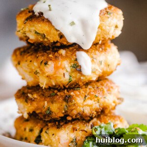 Stacked coconut shrimp cakes topped with sauce, ready to be served.