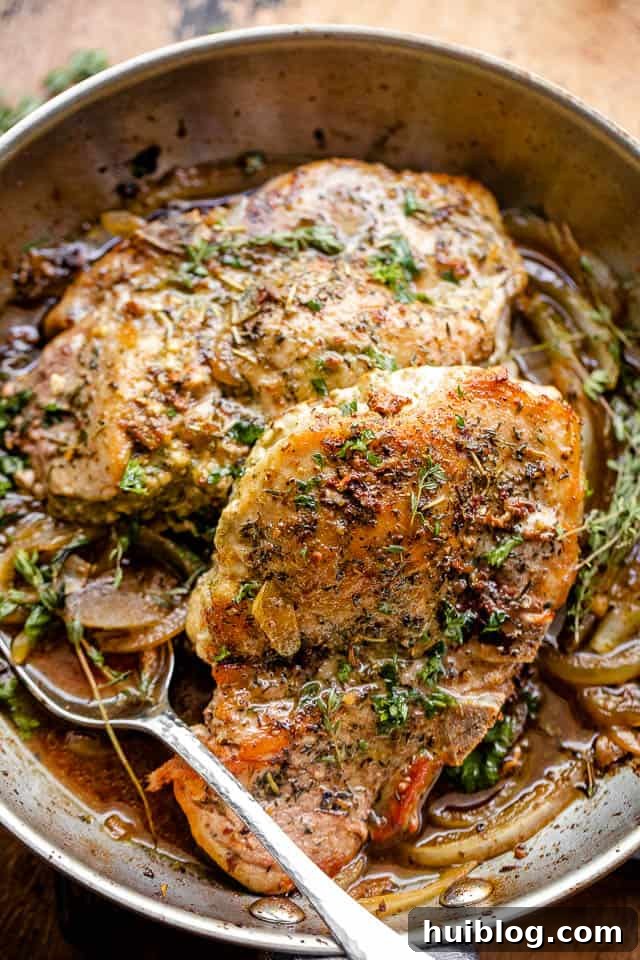 overhead close-up shot of two pesto stuffed pork chops in a cast iron skillet, garnished with fresh herbs
