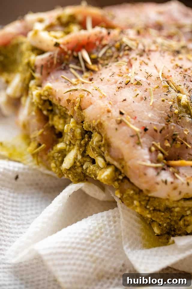 side shot of an uncooked pork chop being prepared, with a pocket cut and ready for pesto and feta cheese stuffing