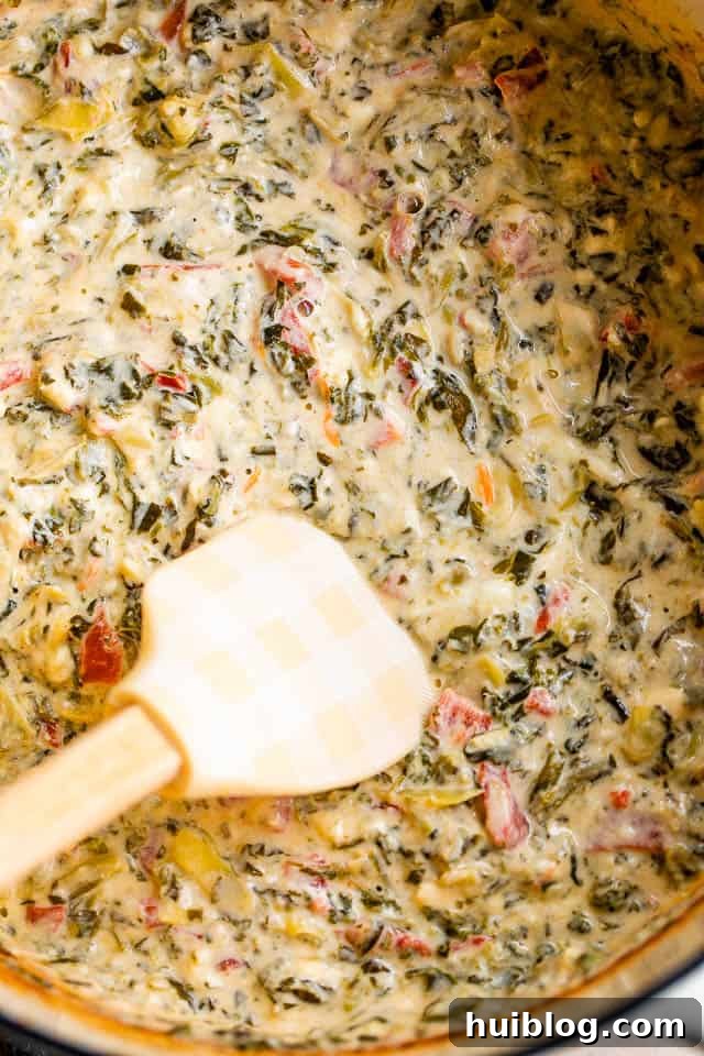 Close-up shot of spinach artichoke dip being stirred with a spatula in a slow cooker