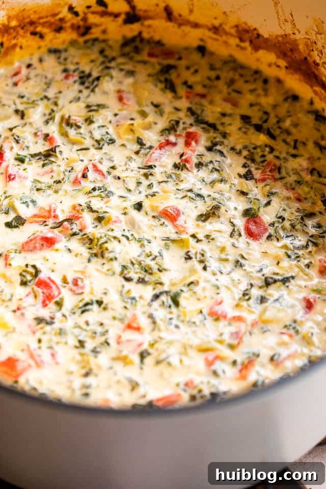 Side view of spinach artichoke dip bubbling in a slow cooker, garnished with fresh herbs