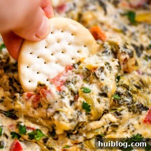 Dipping a round cracker in spinach artichoke dip