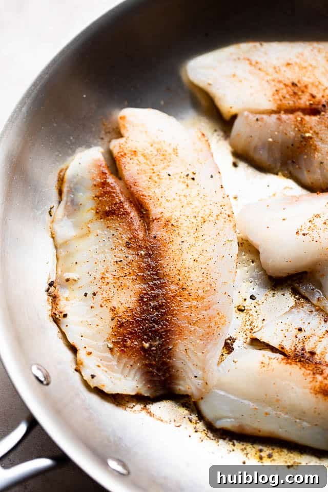 Tilapia fillets sizzling in a hot skillet with a golden-brown crust, ready to be flipped.
