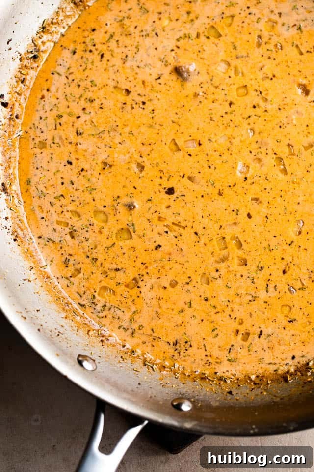 Rich, creamy tomato sauce simmering gently in a stainless steel skillet, releasing aromatic steam.